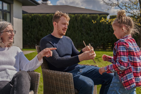 Positive grandfather, her son and granddaughter playing at the garden near the house