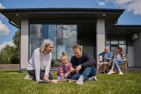 Little kid girl spending time with her daddy and grandmother while sitting at the grassy lawn