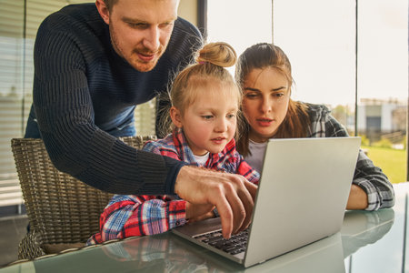 Man pointing at the laptop screen while spending time with his wife and adorable little daughterの写真素材