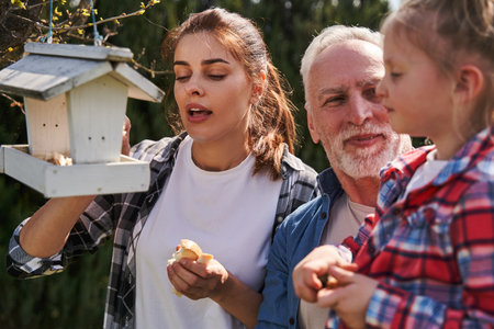Cheerful woman holding bread while feeding birds with her father and daughter