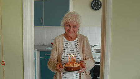 Senior white haired lady bringing cake with candles to husbandの写真素材