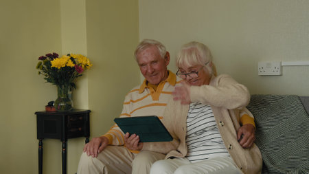 Happy old senior retired grandparents using digital tablet sitting on couch at homeの写真素材