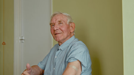 Happy senior man sitting in the doctors office and showing his arm with adhesive plasterの写真素材