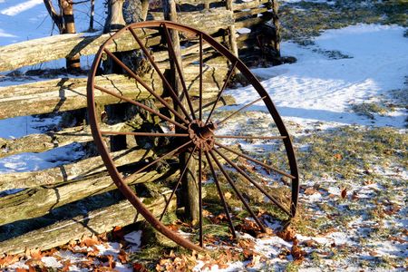 Old rusty iron wheel leaning against a wood split-rail fence, winter scene, not much snow.の写真素材