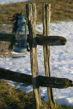 An old oil lamp hanging from a wood fence post, some snow in the background.の写真素材