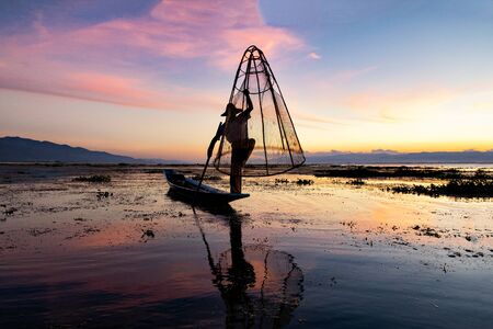 Silhouette Fisherman fishing with big net at Sunset in Inle Lake, Shan State, Myanmarの写真素材