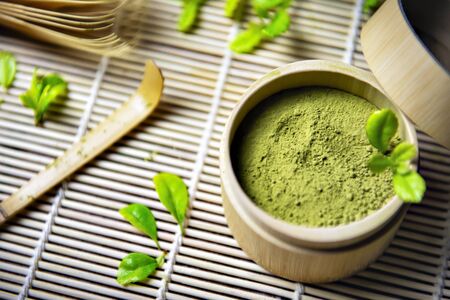 Green Tea Matcha Powder in the Bamboo Cup with Wooden Chasen and Wooden Spoon and on Wooden...