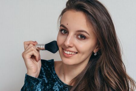 Beautiful young woman in shiny green dress applying powder with a brush to the face.
