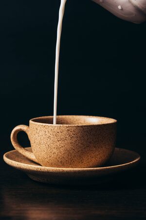 Milk is pouring into a cup of coffee on a black background.の写真素材