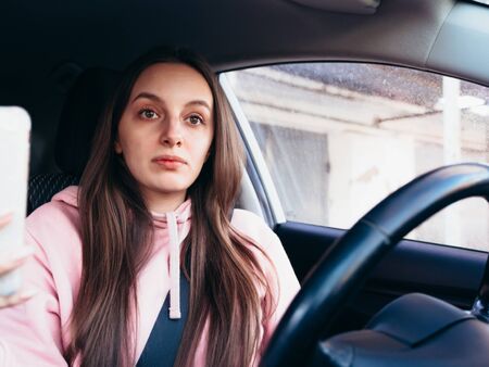 Young girl in pink pite speaks on the phone while sitting in a car.の写真素材