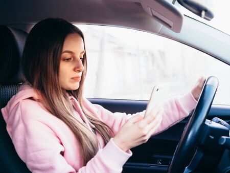 Young girl in pink pite speaks on the phone while sitting in a car.の写真素材