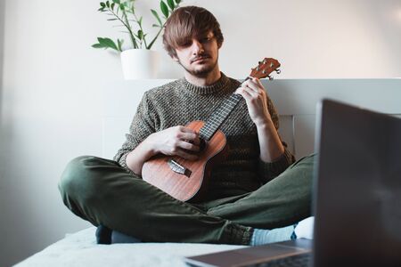 Man sitting at home learns to play ukulele using online lessons.の写真素材