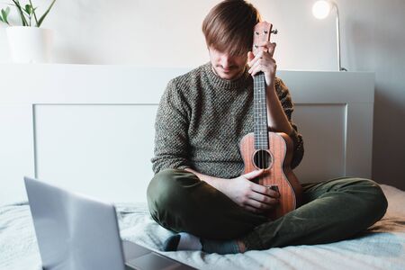 Man sitting at home learns to play ukulele using online lessons.の写真素材