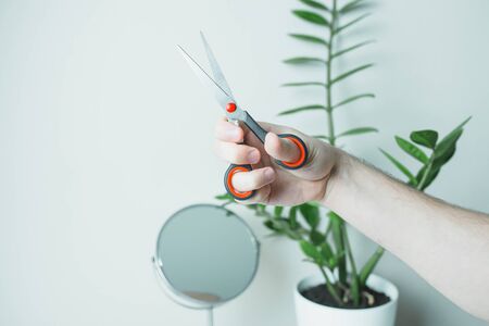 Male hand with scissors opposite the mirror. Stay home.の写真素材
