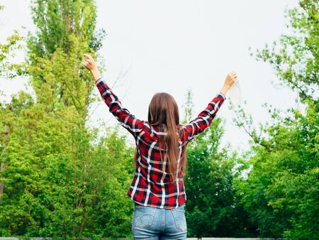 Happy young girl takes off a medical mask and breathes fresh air in nature. Rejoices over the end of the coronavirus pandemic and isolation. Back view.の写真素材