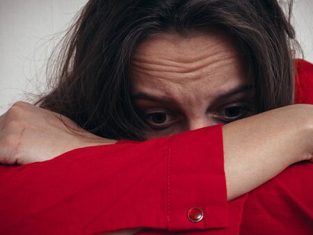 A girl in a red shirt and jeans sits sad against the wall. Domestic violence.
