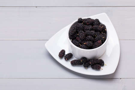 Fresh Black Mulberries in ceramic bowl on grey wooden background, selective focusの写真素材