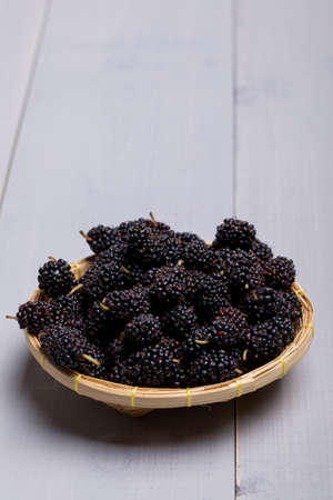 Fresh Black Mulberries in basket on wooden background, selective focus