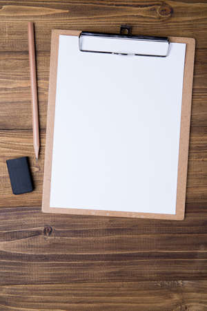 Top view of brown clipboard with white sheet, pencil and eraser on wooden background, use for mock up branding identityの写真素材