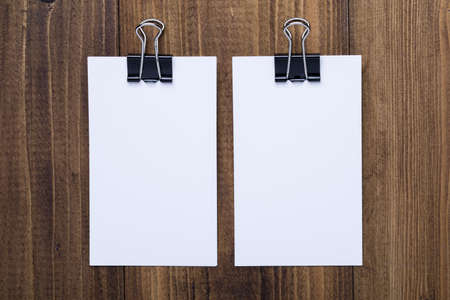 Top view of White paper with black clip on dark wooden background, use for mock up branding identity