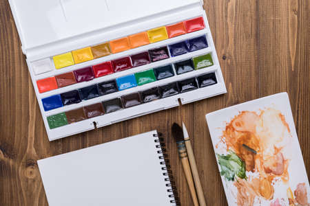 Art supplies (watercolor, palette, brushes and sketchbook) on wooden background with copy spaceの写真素材