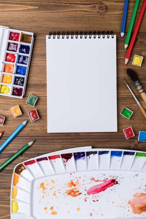 Art supplies (colored pencils, watercolor, palette, brushes) on wooden background with copy spaceの写真素材