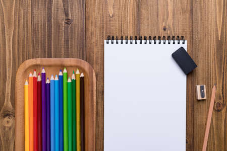 Top view of colored pencils, pencil, sharpener and sketchpad on wooden background.の写真素材