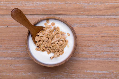 Fresh yogurt on wooden bowl with granola, top viewの写真素材