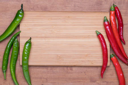 Large red chili and chili spur pepper (large green chili) with chopping board on wooden background, top viewの写真素材