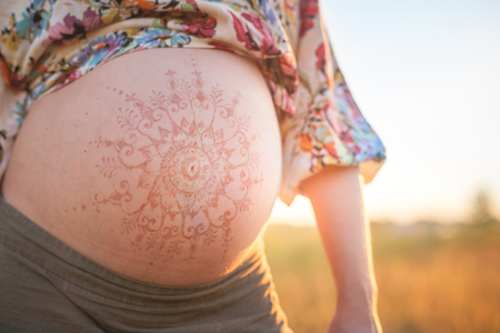 A beautiful pregnant woman on the beach touching her mehandi ornament belly with love and care at sunset lights summer eveningの写真素材