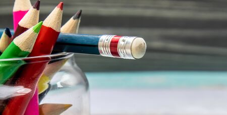 Bottom pencils with an eraser and multi-colors pencils against the brown wood grain background