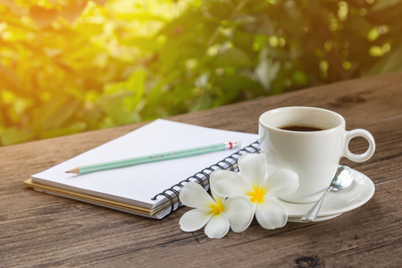 Coffee and a notebook on wooden table with warm sunlight in a gardenの写真素材