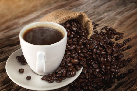 A cup of hot coffee on a wooden table with roasted coffee beans