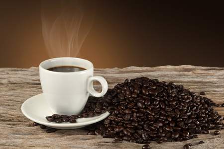 A cup of hot coffee on a wooden table with roasted coffee beansの写真素材