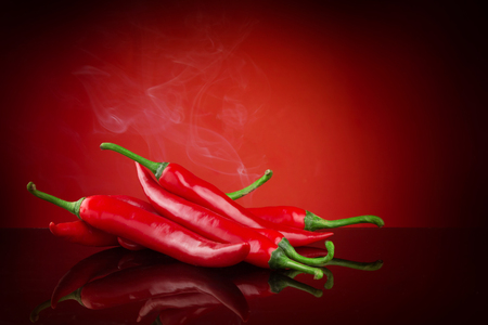 Red hot chili on red background with reflection and smoke and copy space suitable for article or graphic designの写真素材