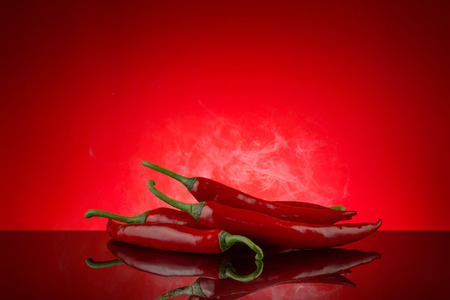 Red hot chili on red background with reflection and smoke and copy space suitable for article or graphic designの写真素材