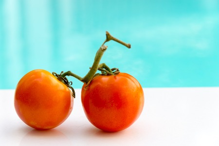 light red tomato on white floor with blue sky swimming pool backgroundの写真素材