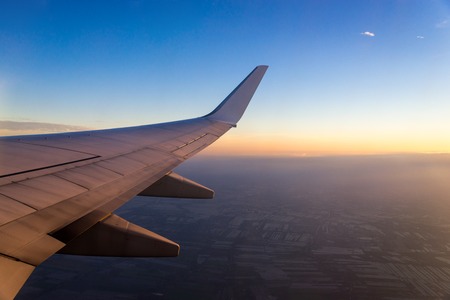 Wing of the air plane on the sea of cloud sunset sky background from window airplaneの写真素材