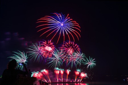 woman watching /  take a photo firework new year, beautiful colorful firework with light reflex in water display for celebration happy new year and merry christmas in the night sky, pattaya city, thailandの写真素材
