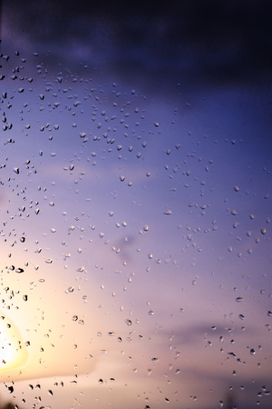Rain / Water drop of rain on glass with sky outdoor background with  sunset / sun rise light effect (colorful light) on glassの写真素材