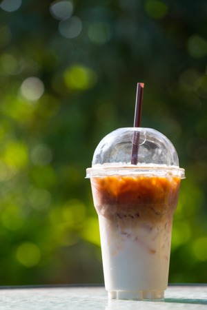 iced coffee in plastic cup / ready to go package on wood and green bokeh blured background garden outdoor.の写真素材