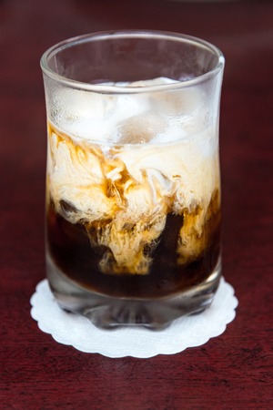 iced coffee pouring with cream milk in glass on wood red table background and texture