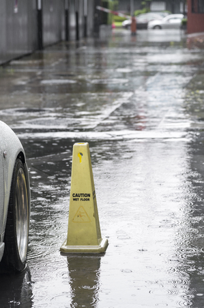 close up raindrops / water drop flooding on street floor and warning sign "caution wet floor" in parking car.の写真素材