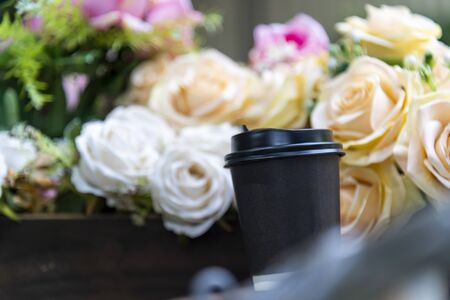 Paper coffee cup on bouquet of flowers and green outdoor backgroundの写真素材