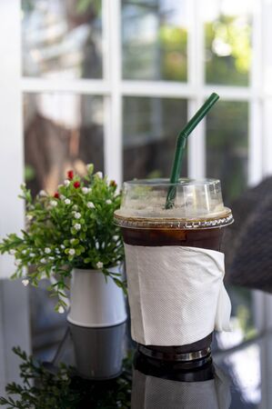 Iced Americano coffee in take home plasttic cup on white table
and window view with green outdoor backgroundの写真素材