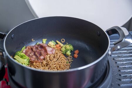 Stir-fry Instant noodles korean hot chili ramen stlye with smoke pork bacon in cooking pan.