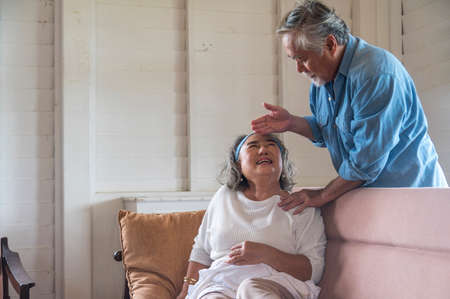 Asian senior husband take care and comforting ill wife in living room .- retired elder lover couple lifestyleの写真素材