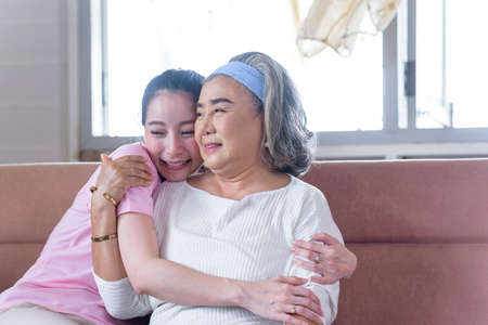Asian young woman take care and  support with hug, that make feel good and smile older mother in living room. family conceptの写真素材