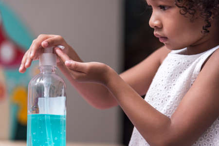 Little African American girl child put alcohol gel sanitizer pump on Hands  for cleaning /wash his hands before wear face mask on faceの写真素材