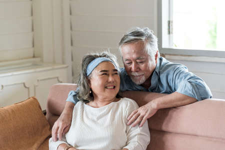 Asian senior husband hug relax and smile wife take care in living room .- retired elder lover couple lifestyleの写真素材